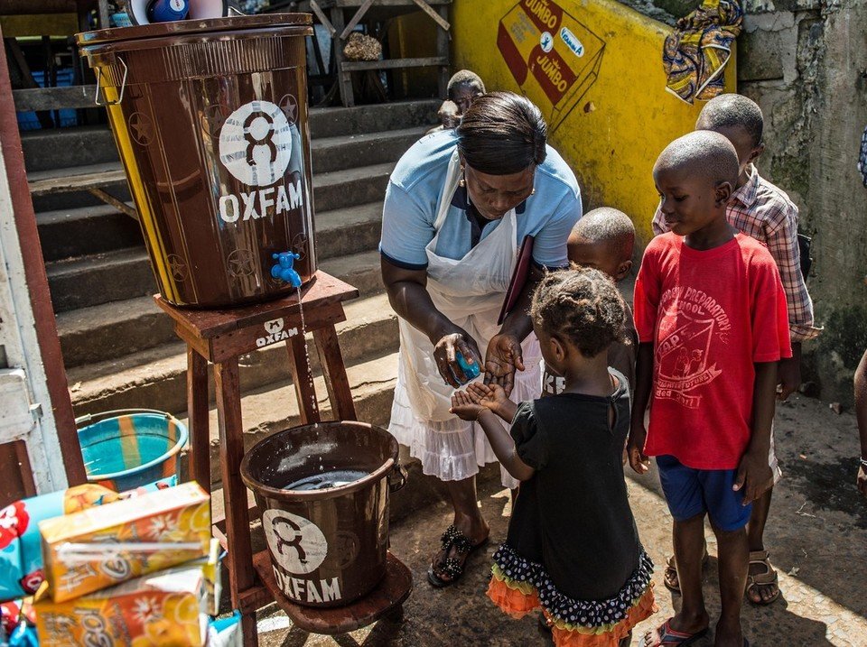 Photo: Tommy Trenchard / Oxfam Community health worker Marrion Thomson teaches children how to wash their hands at an Oxfam Hand Washing Point in Congo Town, an area in Freetown, Sierra Leone.